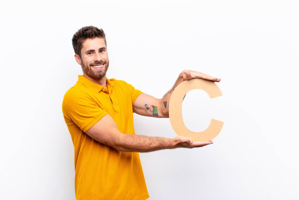 young handsome man excited, happy, joyful, holding the letter C of the alphabet to form a word or a sentence. - Фото, зображення