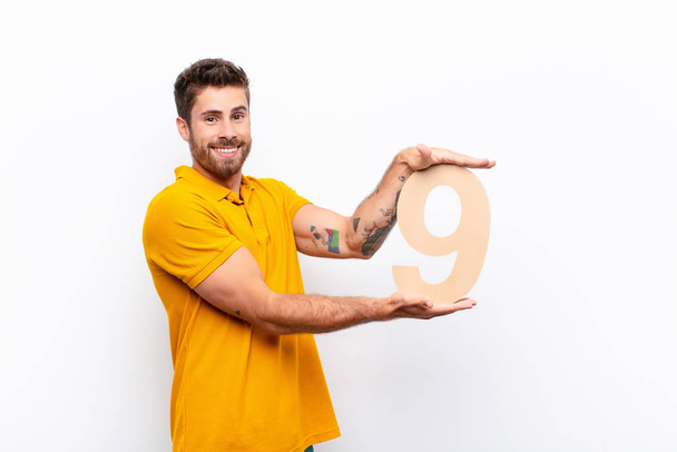 young handsome man excited, happy, joyful, holding a number 9. - Φωτογραφία, εικόνα