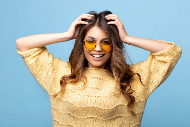Attractive young woman in yellow sweater posing on blue background. Pretty girl in yellow glasses. - Foto, Imagem