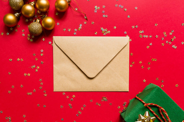 Christmas composition. Envelope, wrapped gift, toys on red background with golden confetti. new year concept. Greeting card, xmas celebration 2020. Flat lay, top view, copy space, mockup - Photo, image