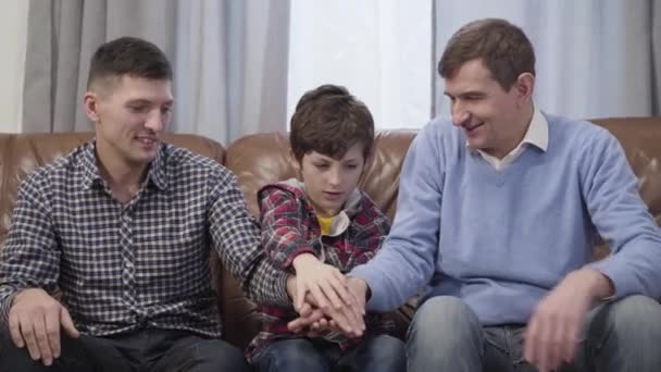 Happy Caucasian family putting hands on top of each other and raising them up. Smiling cheerful father, son, and grandfather spending evening together indoors. Unity, lifestyle, happiness. - Footage, Video