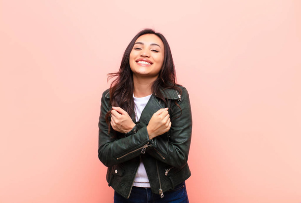 young latin pretty woman smiling cheerfully and celebrating, with fists clenched and arms crossed, feeling happy and positive against flat wall - Foto, imagen