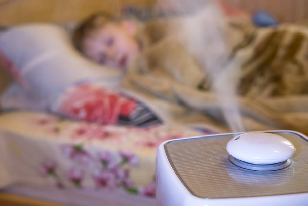 steam flow from a humidifier and an air ionizer in a blurred room with a sleep small child. Climatic device used to increase indoor humidity. respiratory disease prevention - Foto, Imagem