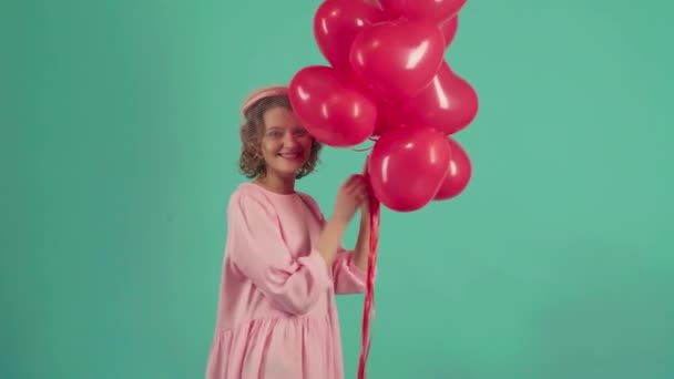 Valentine girl with red air balloons laughing, on green background. Happy Young woman celebrating Valentines Day. Holiday party. - Filmagem, Vídeo