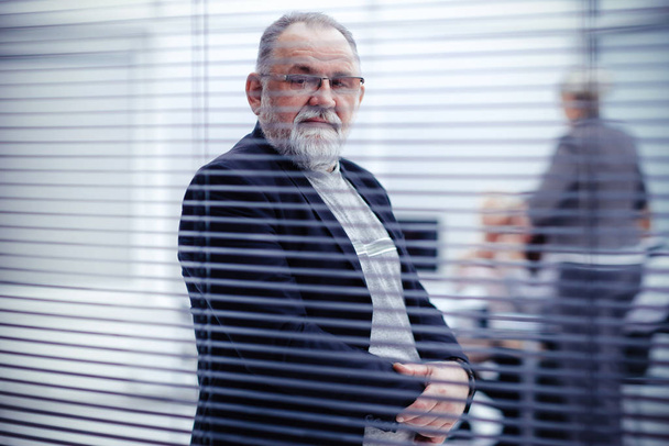 through the blinds. elderly confident businessman standing in front of office window. - 写真・画像