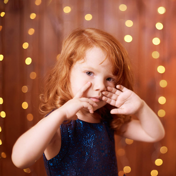 Christmas happy girl. Luxury attractive red hair child. Xmas miracle. Green tree, lights, bokeh - Photo, Image