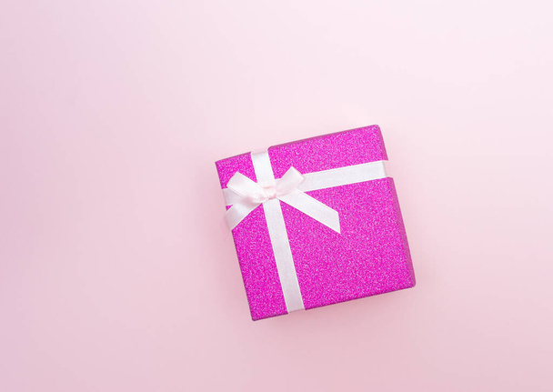 Flatlay with bright pink gift box with white atlas ribbon on pink background - 写真・画像
