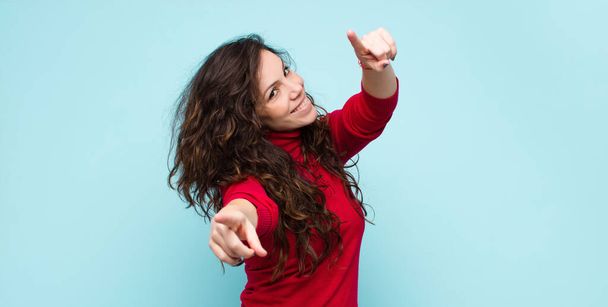 young pretty woman feeling happy and confident, pointing to camera with both hands and laughing, choosing you against blue wall - Fotoğraf, Görsel