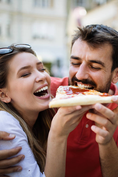 Happy couple laughing and eating pizza, having a great time together - Fotó, kép