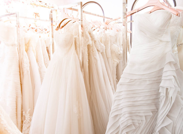 Beautiful, white bridal dress texture on background. Wedding dresses hanging on a hanger interior of bridal salon. Design, fashion modern luxury in detail. Soft  focus with warm light. - Foto, Bild