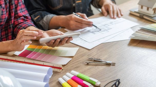 Дизайнер интерьера и архитектор выбирают цвет в цветовых образцах графика для выбора окраски дома в офисе с чертежом. Концепция строительства. - Фото, изображение