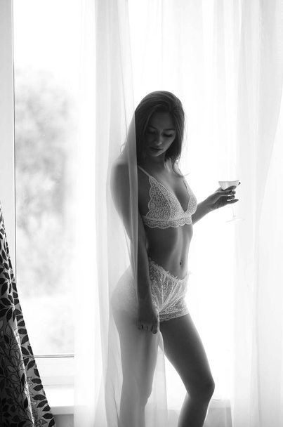 Krásná mladá brunetka žena v něžné erotické bílé spodní prádlo v blízkosti velkého ranního okna. - Fotografie, Obrázek