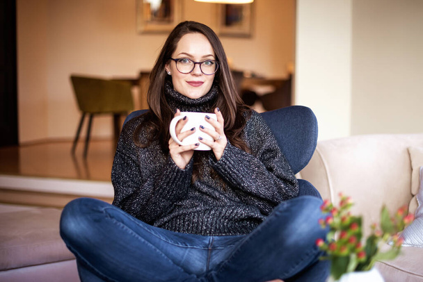 Evdeki koltukta dinlenirken çayını içen çekici genç bir kadının portresi..  - Fotoğraf, Görsel