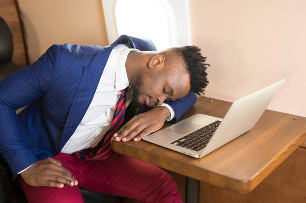 handsome african young man in suit in private jet cabin with laptop - Photo, image