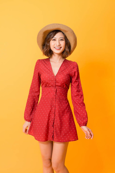 Portrait of young beautiful asian woman  wear red dress and hat over orange background. Summer concept. - Foto, afbeelding