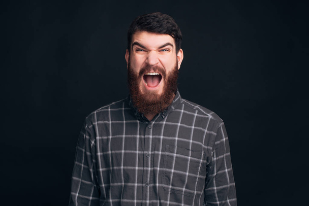 Bearded man is screaming at the camera on dark background. - Photo, Image