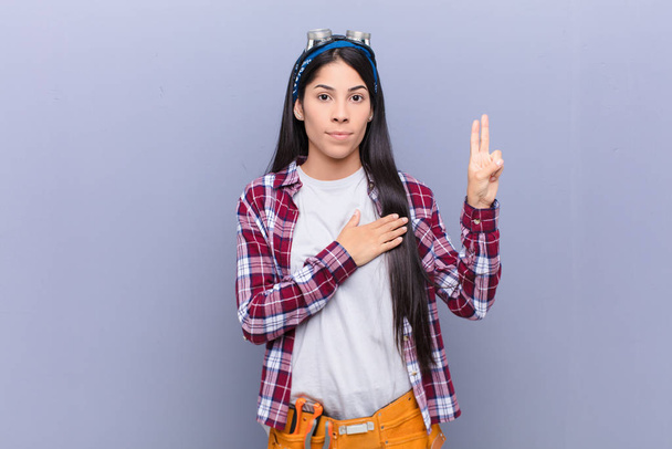 young latin woman looking happy, confident and trustworthy, smiling and showing victory sign, with a positive attitude - Photo, Image