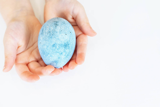 A gyerekkezek húsvéti tojást tartanak. Gyönyörű tojást festettek húsvétra. Egy kék tojás közelsége. - Fotó, kép