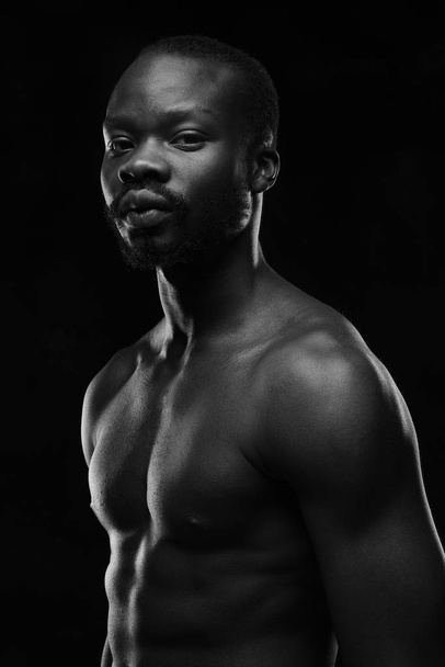 black and white portrait of a handsome black man with naked sports torso looking in the camera on dark background - Фото, зображення