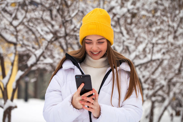 Young beautiful woman with a mobile phone in a winter park - Fotoğraf, Görsel