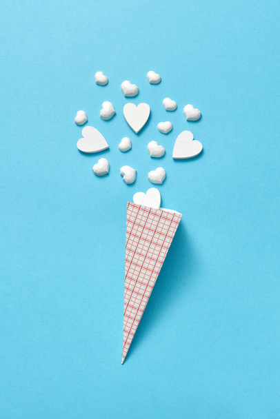 Paper cone with small white gypsum hearts as ice-cream sweet dessert on a pastel blue background with soft shadows, copy space. Valentine's day greeting card. - 写真・画像