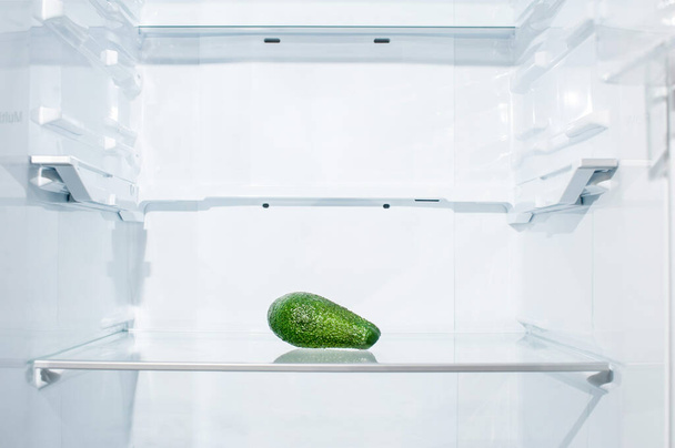 Een avocado ligt op een plank in een lege koelkast - Foto, afbeelding
