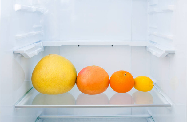 Pomelo, grapefruit, orange and lemon lie on a shelf in the refrigerator - Foto, afbeelding