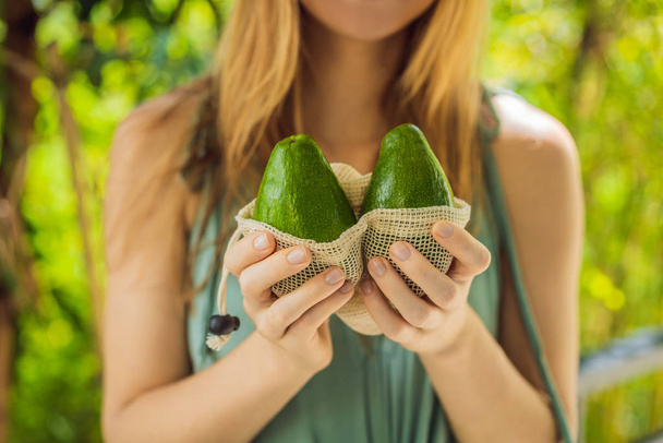 Avocado in a reusable bag in the hands of a young woman. Zero waste concept - Фото, изображение
