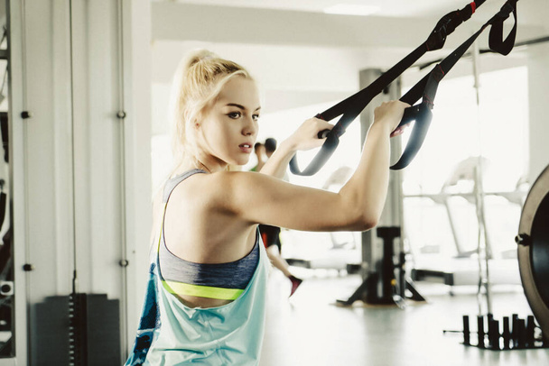 Sporty woman doing TRX exercises in the gym - Photo, Image
