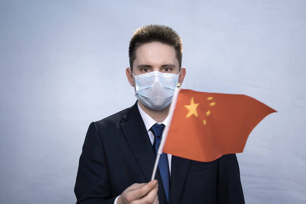 Portrét mladého muže v obleku a lékařské masce s čínskou vlajkou v rukou. Individuální ochrana kancelářských pracovníků před epidemiemi a viry, osobní bezpečnostní nástroje. - Fotografie, Obrázek