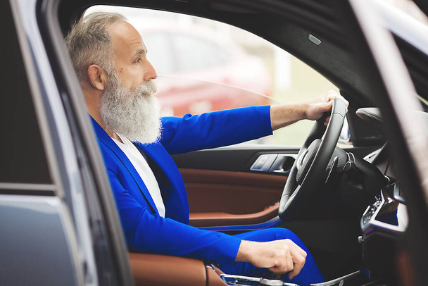 Old handsome man inside the car. Bearded mature male in the automobile. Confident businessman buying the car. - Фото, зображення