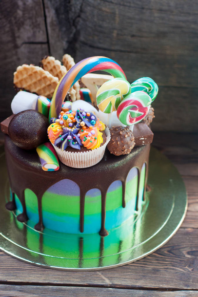 Green and blue birthday cake with melted chocolate, cupcake, cake pops, candies, lollipops, waffles and sprinkles.  - Фото, изображение