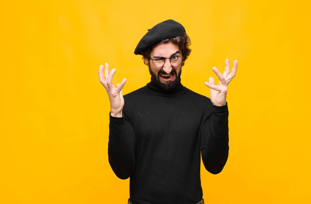 young french artist man screaming with hands up in the air, feeling furious, frustrated, stressed and upset against orange wall - Fotografie, Obrázek