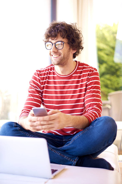 Shot of happy man wearing casual clothes and glasses while text messaging at home.  - Foto, Bild