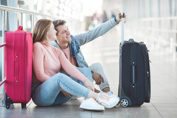 空港ターミナルの幸せな若いカップルは、彼らの飛行を待っている間に楽しみを持っています。二人の男と女が旅行に行く. - 写真・画像