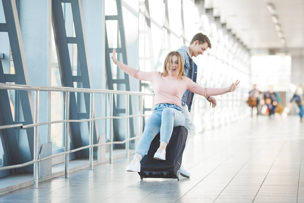 Jovem casal feliz no terminal do aeroporto se divertindo enquanto espera por seu voo. Duas pessoas homem e mulher vão tropeçar
. - Foto, Imagem