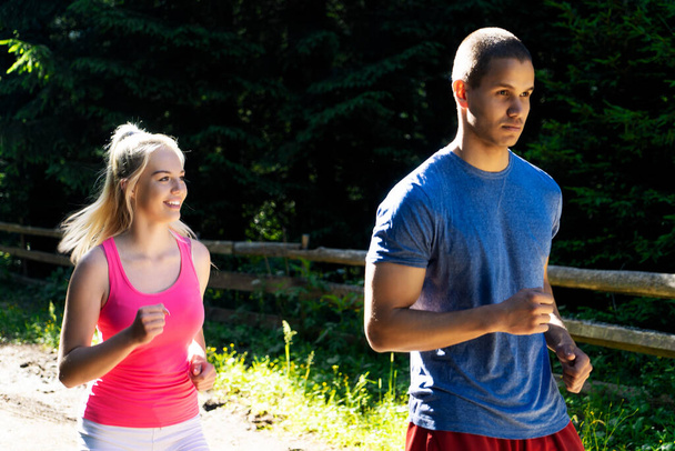 Running γυμναστήριο ζευγάρι των δρομέων κάνει αθλητισμό στο δρόμο εξωτερική. Ενεργό διαβίωσης άντρας και γυναίκα τζόκινγκ προπόνηση καρδιο σε εξωτερικούς χώρους καλοκαίρι φύση. - Φωτογραφία, εικόνα