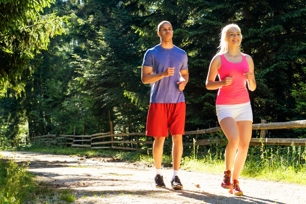 Running fitness couple of runners doing sport on road outdoor. Active living man and woman jogging training cardio in summer outdoors nature. - Fotoğraf, Görsel