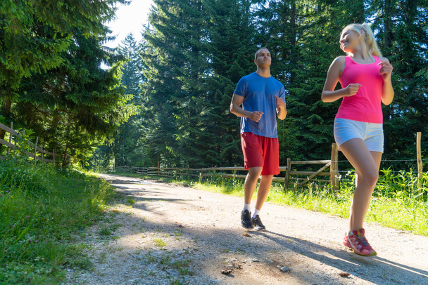 Running fitness couple of runners doing sport on road outdoor. Active living man and woman jogging training cardio in summer outdoors nature. - Foto, Bild