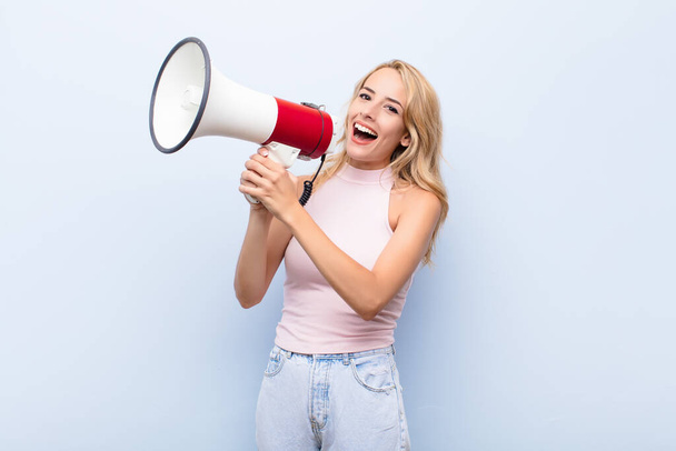 young blonde woman feeling happy, excited and positive, giving a big shout out with hands next to mouth, calling out with a megaphone - Fotoğraf, Görsel