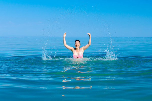 Excited female jumping with widespread hands in shallow sea wate - 写真・画像