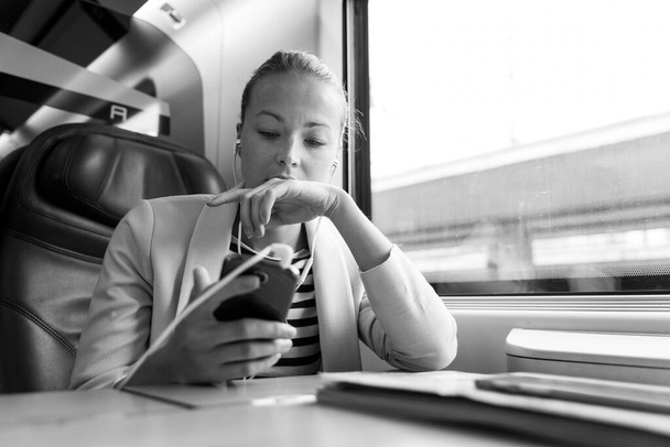 Üzletasszony kommunikál mobiltelefonon, miközben vonattal utazik. - Fotó, kép