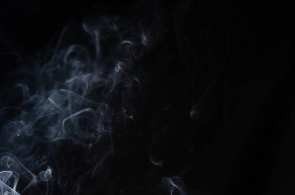 Abstract puffs of smoke on the left side of the frame on a dark background with a place for text, mysticism, fantasy - Photo, image