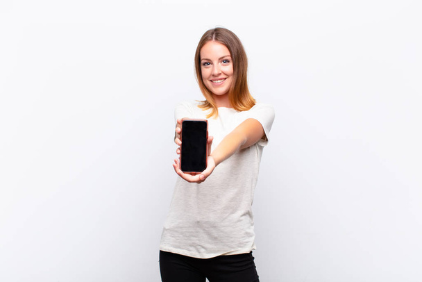 red head pretty woman smiling happily with friendly, confident, positive look, offering and showing an object or concept holding a smartphone - Foto, Bild