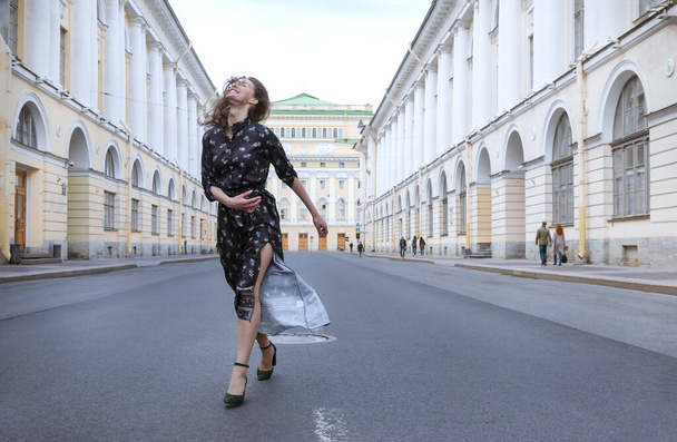1 young woman in a brown dress walks down the street against the - Zdjęcie, obraz