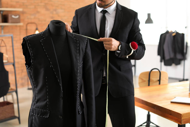 Jonge kleermaker metingen van mannelijke jas op etalagepop in atelier - Foto, afbeelding