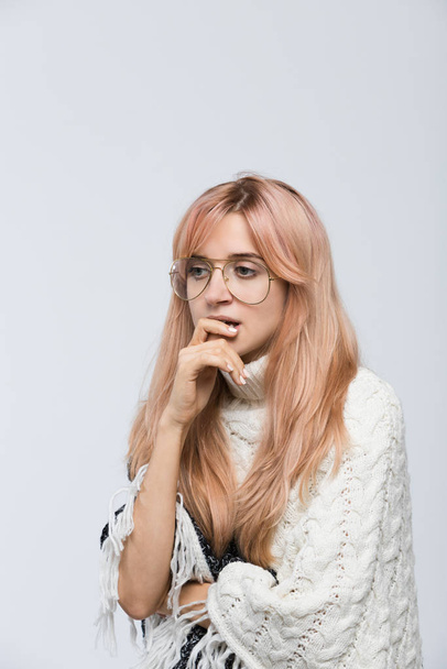 Studio portrait of cute student in white sweater with eyewear doubting with thoughtful face expression, presses hand to mouth/plans something on coming weekends/woman remember something. - Fotoğraf, Görsel