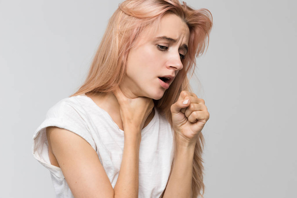 Retrato de estudio recortado de una joven estudiante malsana que tose sosteniendo su garganta / sufre de resfriado y gripe, tos, dolor de garganta, malestar, dolor de pecho, medicina y concepto de atención médica
. - Foto, imagen