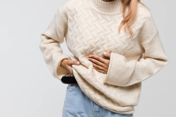 Close-up shot of woman in white sweater suffering from abdominal pain, having menstruation pain, feels bad, front view. Menstrual period, gynecology, gastritis, healthcare, medical concept. - Foto, Imagen
