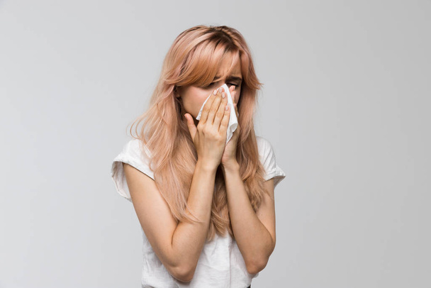 Portrait of young beautiful woman blowing her nose into a paper napkin, closed eyes/sneezing, allergy symptoms, flu, rhinitis, cold, sickness, desperately sick, healthcare and medicine concept. - Foto, Bild